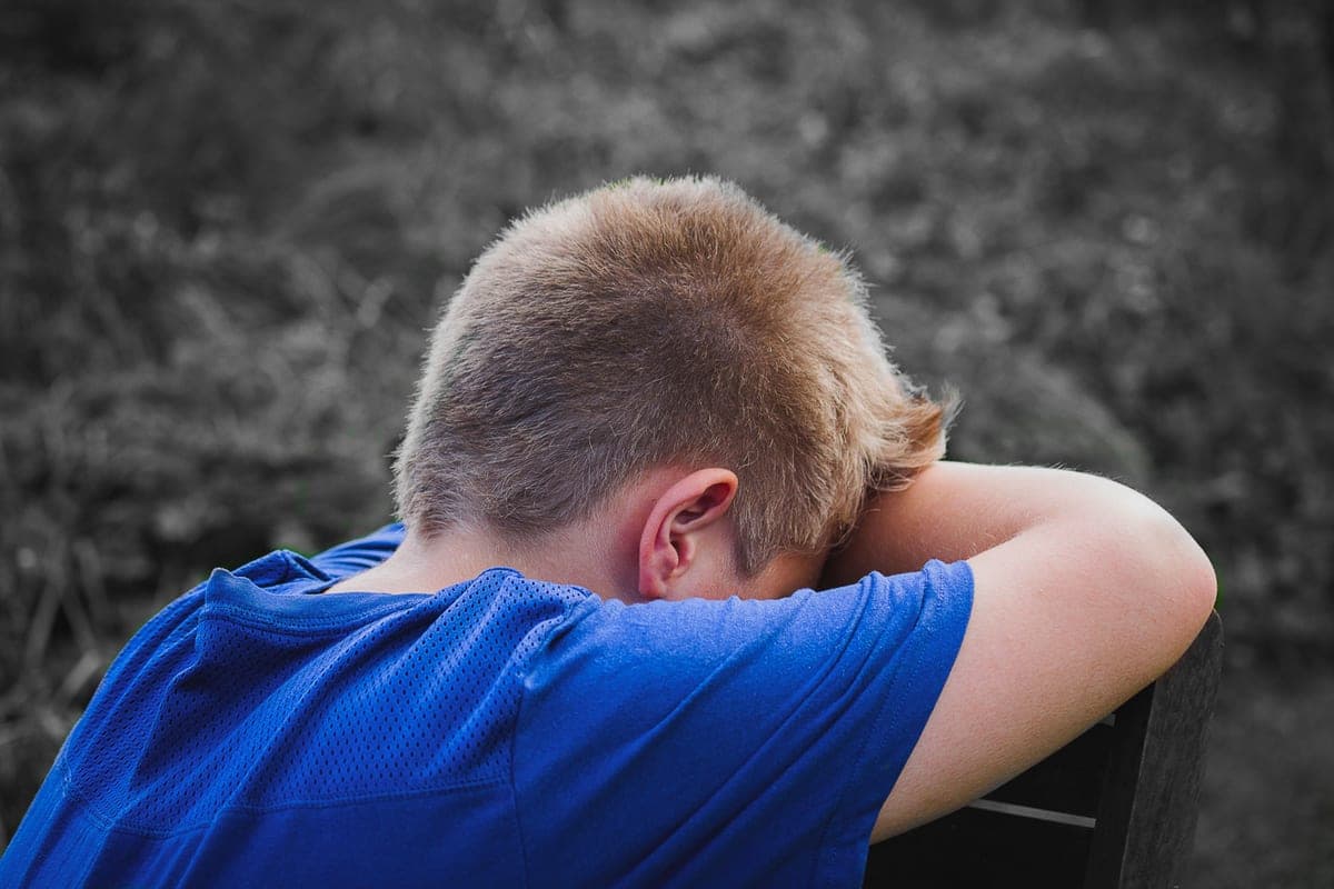 A child resting their head on their arms outdoors, looking disappointed