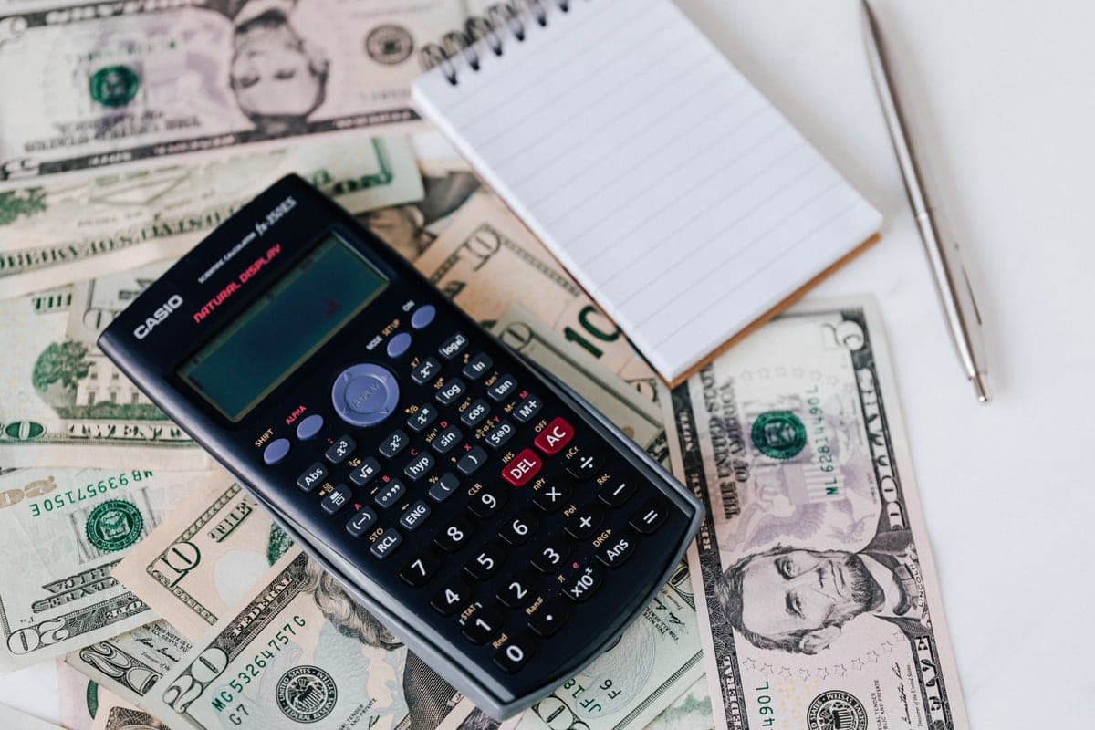 A calculator and notepad on top of US dollar bills, used for budgeting
