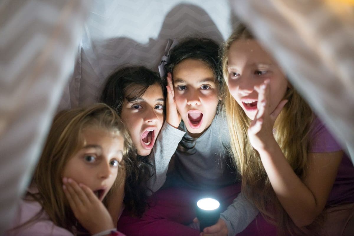 Children under a blanket tent with a flashlight