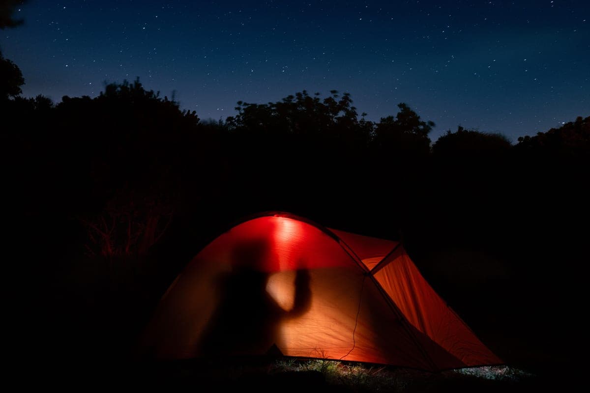 An illuminated tent under a star-filled night sky