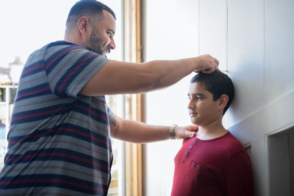 A parent measuring a child's height against a wall at home