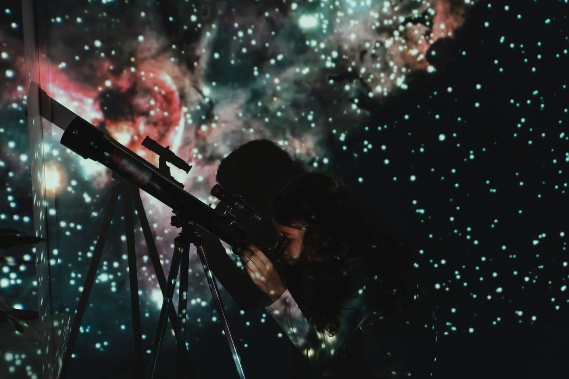 A child looking through a telescope beneath a projected starfield