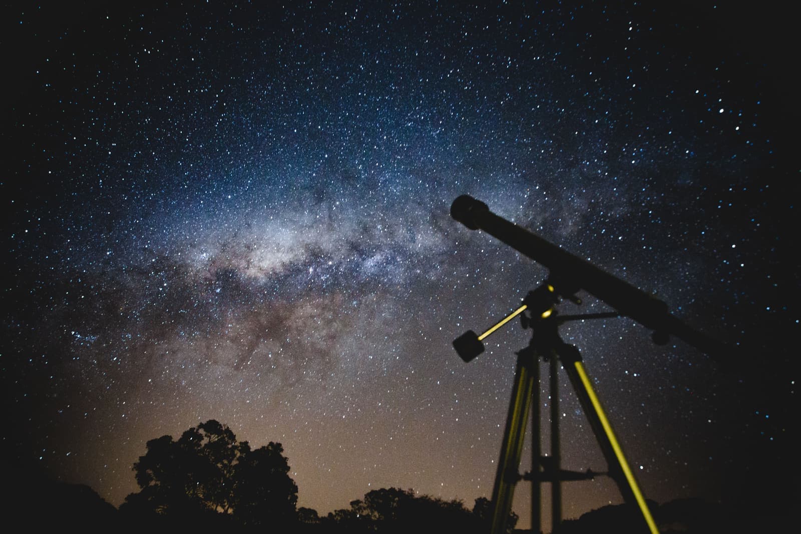 A telescope silhouetted against a deep blue night sky