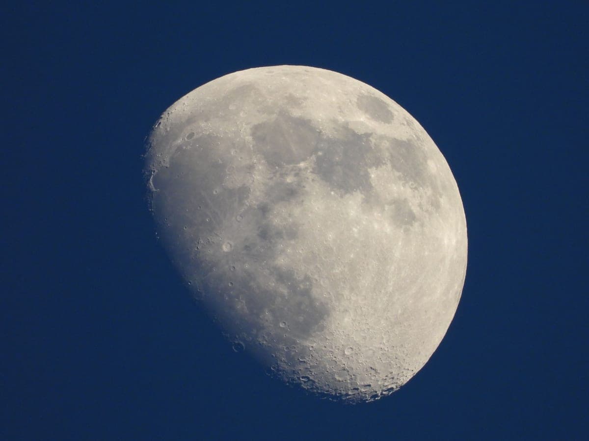 A telescope tube angled up toward the Moon in a twilight sky